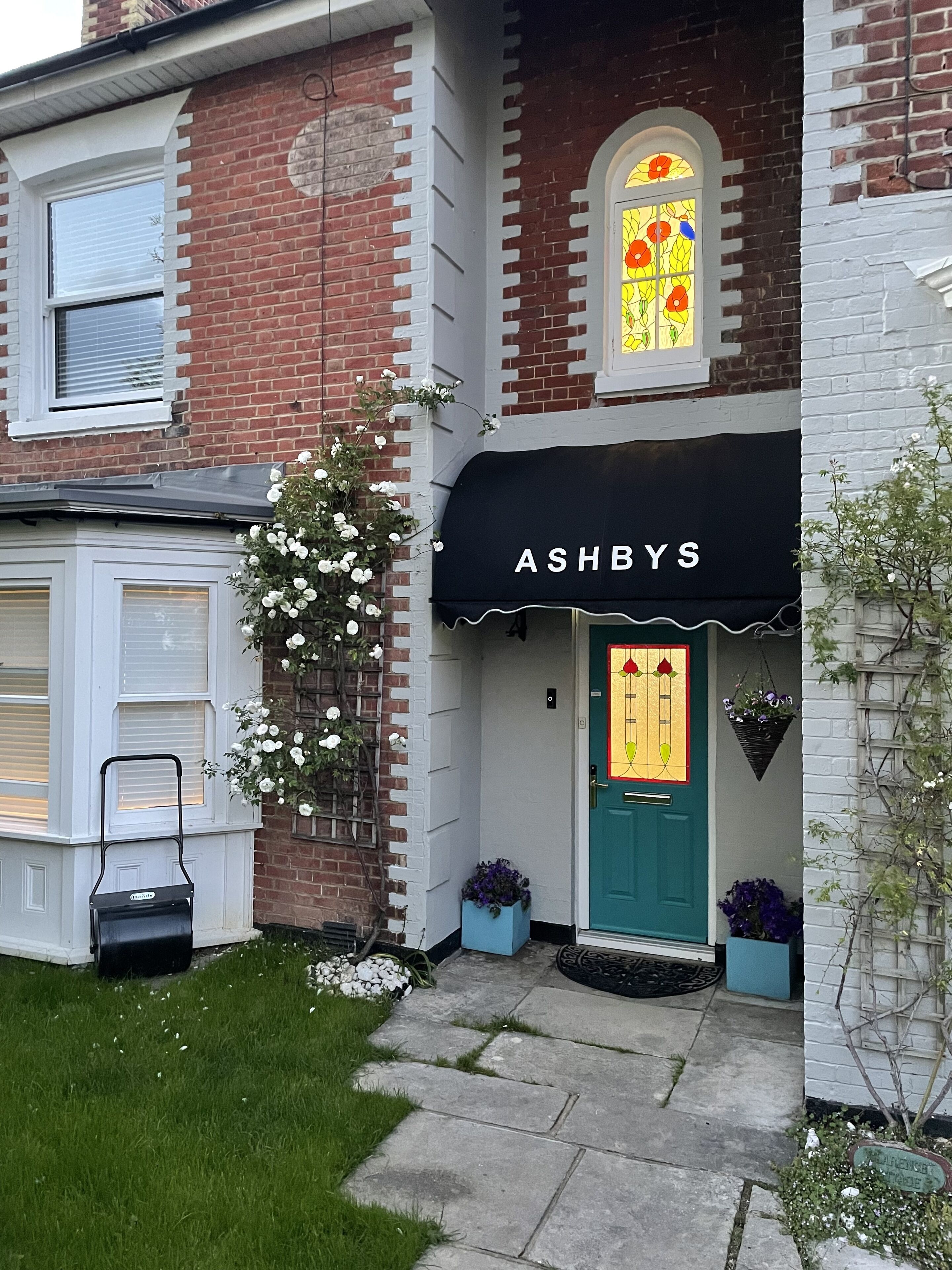 A two-story brick building with a green door and a black awning displaying the name "ASHBYS".