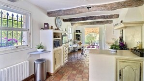Una cocina con vigas de madera a la vista, un ventanal con vistas a la vegetación y una isla central con fregadero y encimera.