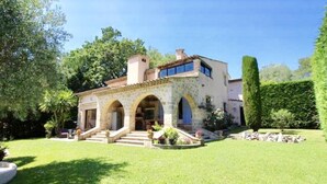 Una casa de piedra de dos pisos con un arco central, una pequeña escalera que conduce a la entrada y un césped bien cuidado.