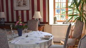 A dining room with striped wallpaper, wooden beams, a table set with plates, glasses, and a vase of flowers.