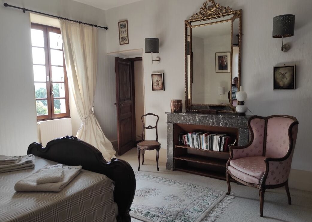 A room with a bed, a chair, a bookshelf, a mirror, and a window with curtains.