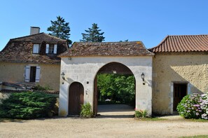 A rustic stone building with a large arched entrance, a small garden with flowers, and a clear blue sky. - Residence in the heart of Perigord with heated pool (Vergt)