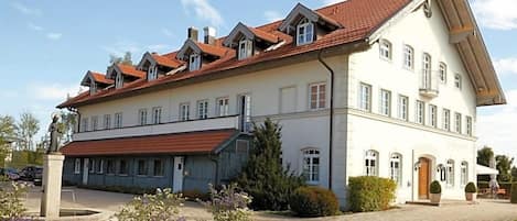 A large two-story building with a red-tiled roof, multiple windows, and a paved courtyard.