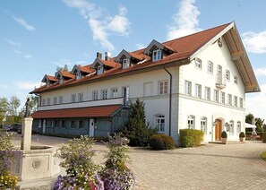 A large two-story building with a red-tiled roof, multiple windows, and a paved courtyard.