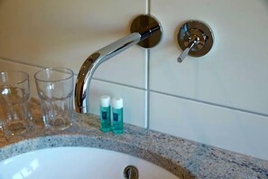 A bathroom sink with a chrome faucet, two clear glasses, and two bottles of blue liquid on the countertop.