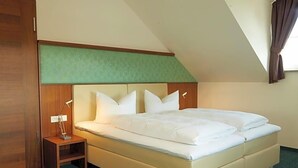 A single bed with a headboard, a bedside table with a lamp, and a window with curtains.