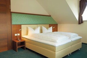 A single bed with a headboard, a bedside table with a lamp, and a window with curtains.