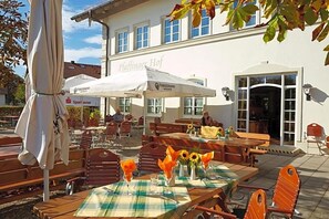 An outdoor seating area with tables and chairs, a white umbrella, and a building with the sign 'Paffinauer Hof'.