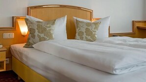 Un lit bien fait, avec une literie blanche et deux coussins décoratifs, une table de chevet avec une lampe et un luminaire fixé au mur.