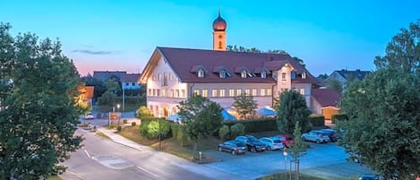A large building with a prominent tower, surrounded by parked cars and trees.