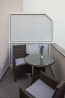 En lille balkon med fletmøbler, et glasbord og en urtepotte med lavendel.