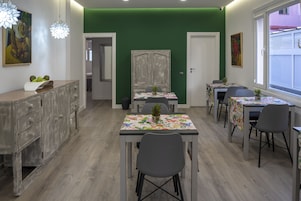 Un espace repas comprenant plusieurs tables et chaises, un meuble avec des tiroirs et un mur d’accent de couleur verte.