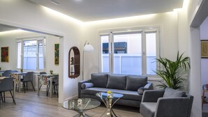 Ein modernes Wohnzimmer mit einem grauen Sofa, einem Glastisch und einem Essbereich mit Stühlen und einem Tisch.