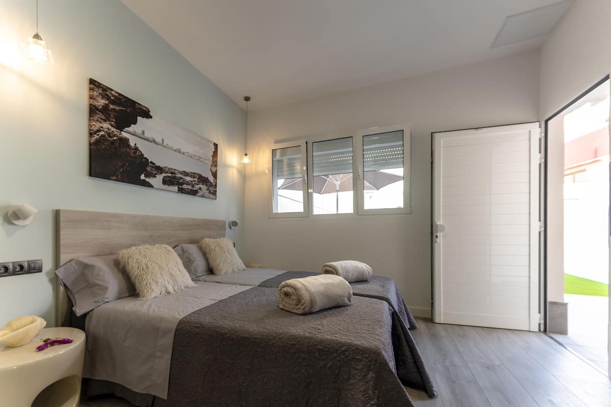 Une chambre avec deux lits, une grande fenêtre et une porte donnant sur un balcon.