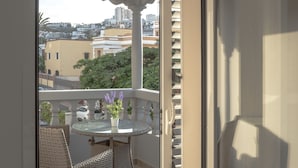 Eine offene Schiebetür führt zu einem Balkon mit Korbmöbeln und einem Glastisch, mit Blick auf eine Stadtlandschaft.