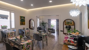 Ein Essbereich mit gedeckten Tischen, ein Wohnzimmer mit Sofa und Couchtisch sowie eine Küchenzeile mit Kaffeemaschine.