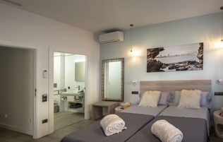 Una moderna camera d'albergo con due letti, bagno e vista su una costa rocciosa.