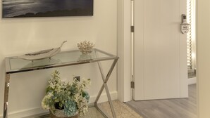 Ein modernes Interieur mit einem Glastisch, einer Zierpflanze und einem Gemälde mit einer Küstenansicht.