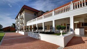 A multi-story hotel with a covered outdoor area, a brick pathway, and a well-maintained garden. - Arcanum Hotel (Bekescsaba)