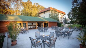 An outdoor patio with multiple tables and chairs, surrounded by potted plants. - Arcanum Hotel (Bekescsaba)
