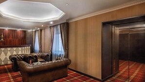 A hotel room with a leather sofa, a plaid carpet, a wooden panel wall, and a modern ceiling design. - Arcanum Hotel (Bekescsaba)