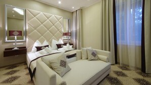 A hotel room with a large bed, a sofa, a mirror, and a window with curtains. - Arcanum Hotel (Bekescsaba)
