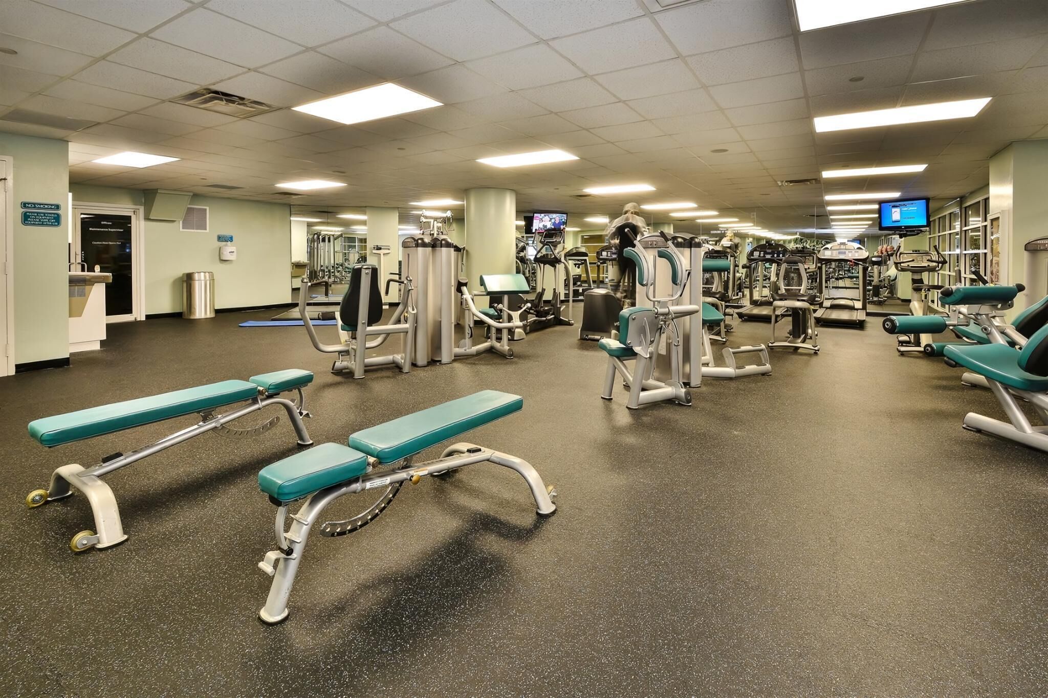 A gym with various exercise equipment, including treadmills and weight machines, and benches.