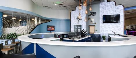 A modern reception area with a curved counter, black chairs, a TV screen, and decorative hanging lights.