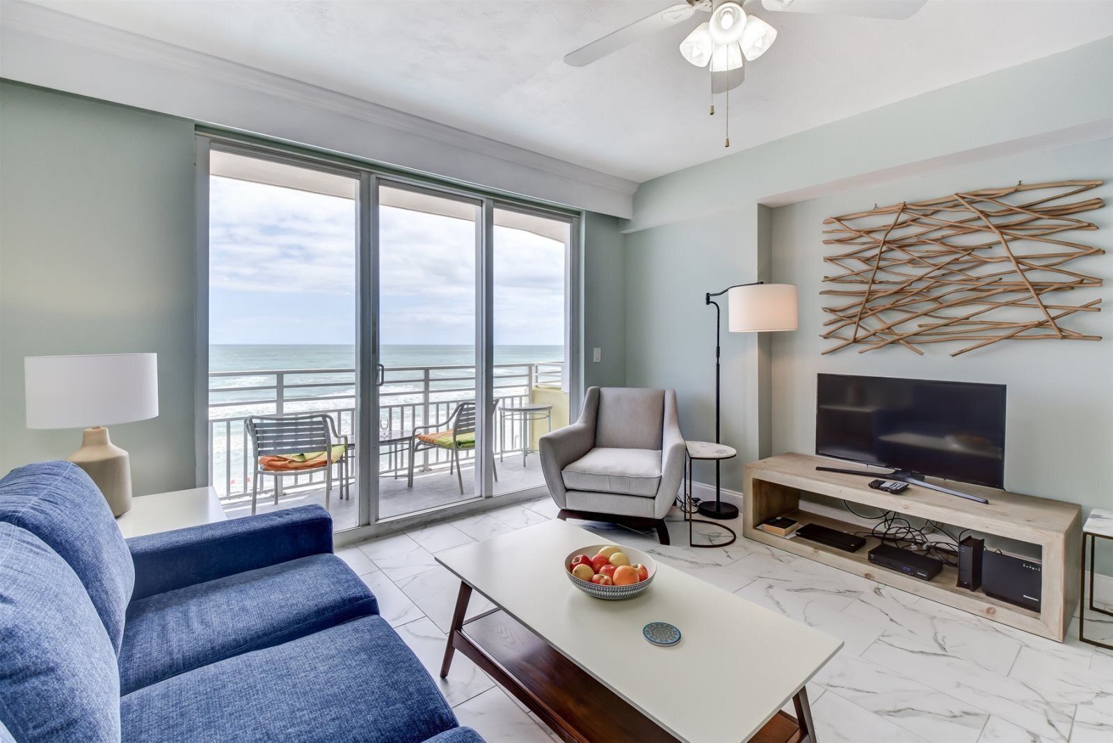 A modern living room with a sofa, a TV, and a balcony with ocean views.