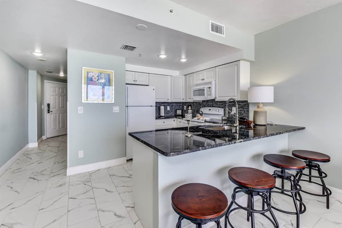 A modern kitchen with a marble floor, white cabinets, a black granite island, and bar stools.