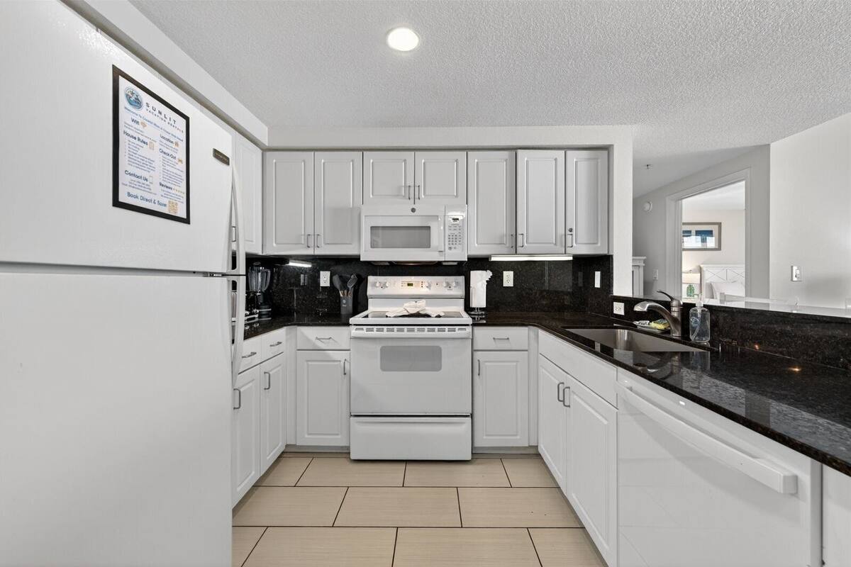 A modern kitchen with white cabinets, a black countertop, a built-in microwave, and a stove.