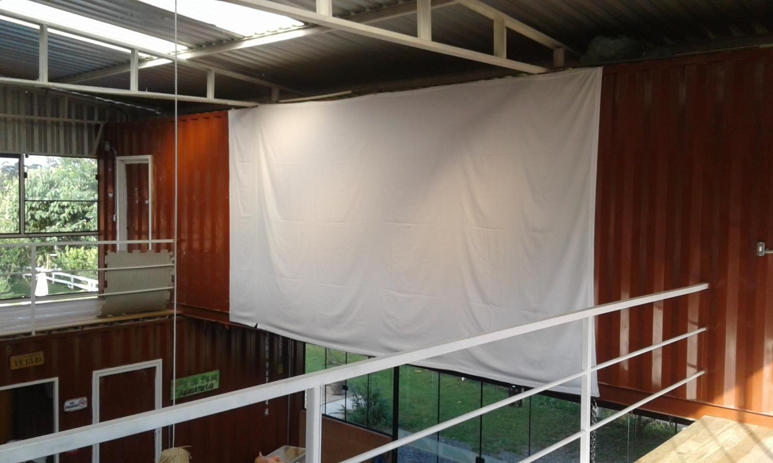 A room with a large white curtain, metal beams, and a view of greenery outside.