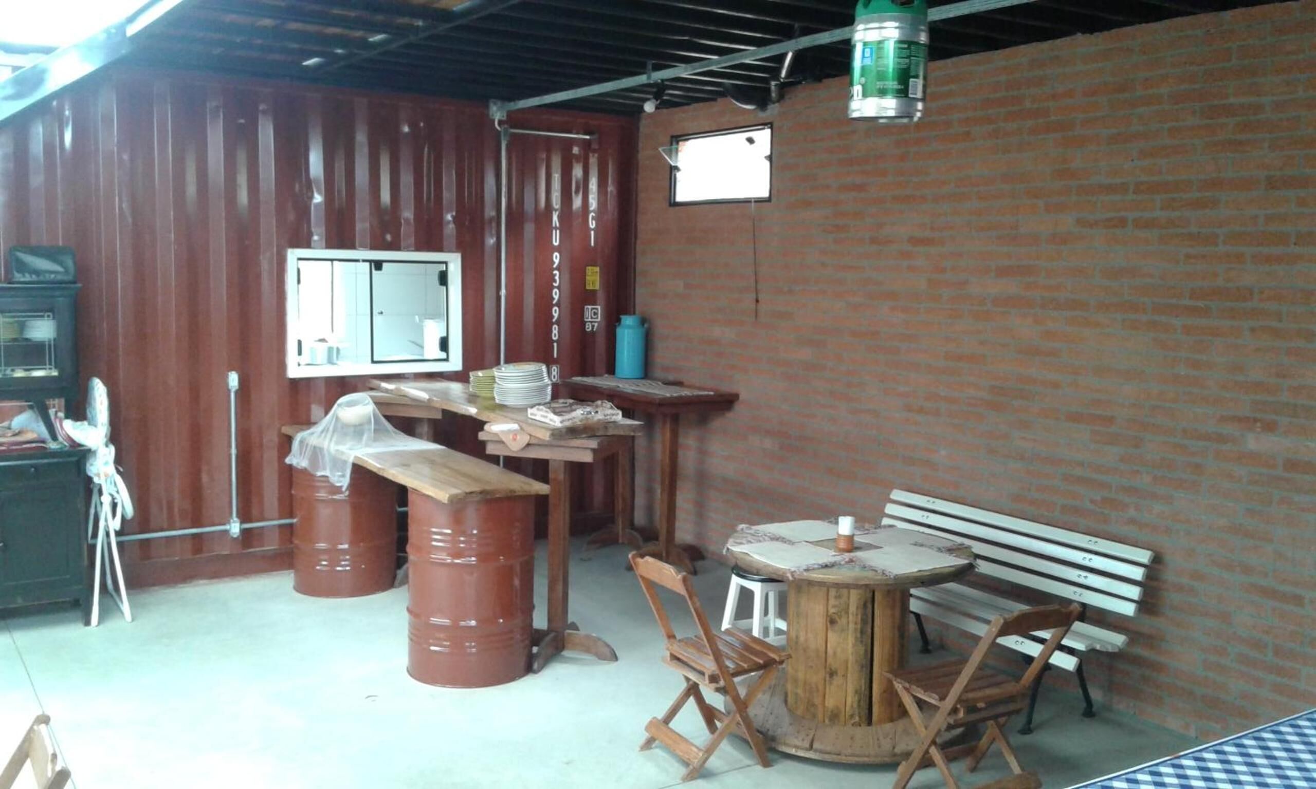 A rustic room with wooden walls, a brick wall, a window, a table with chairs, and a bench.