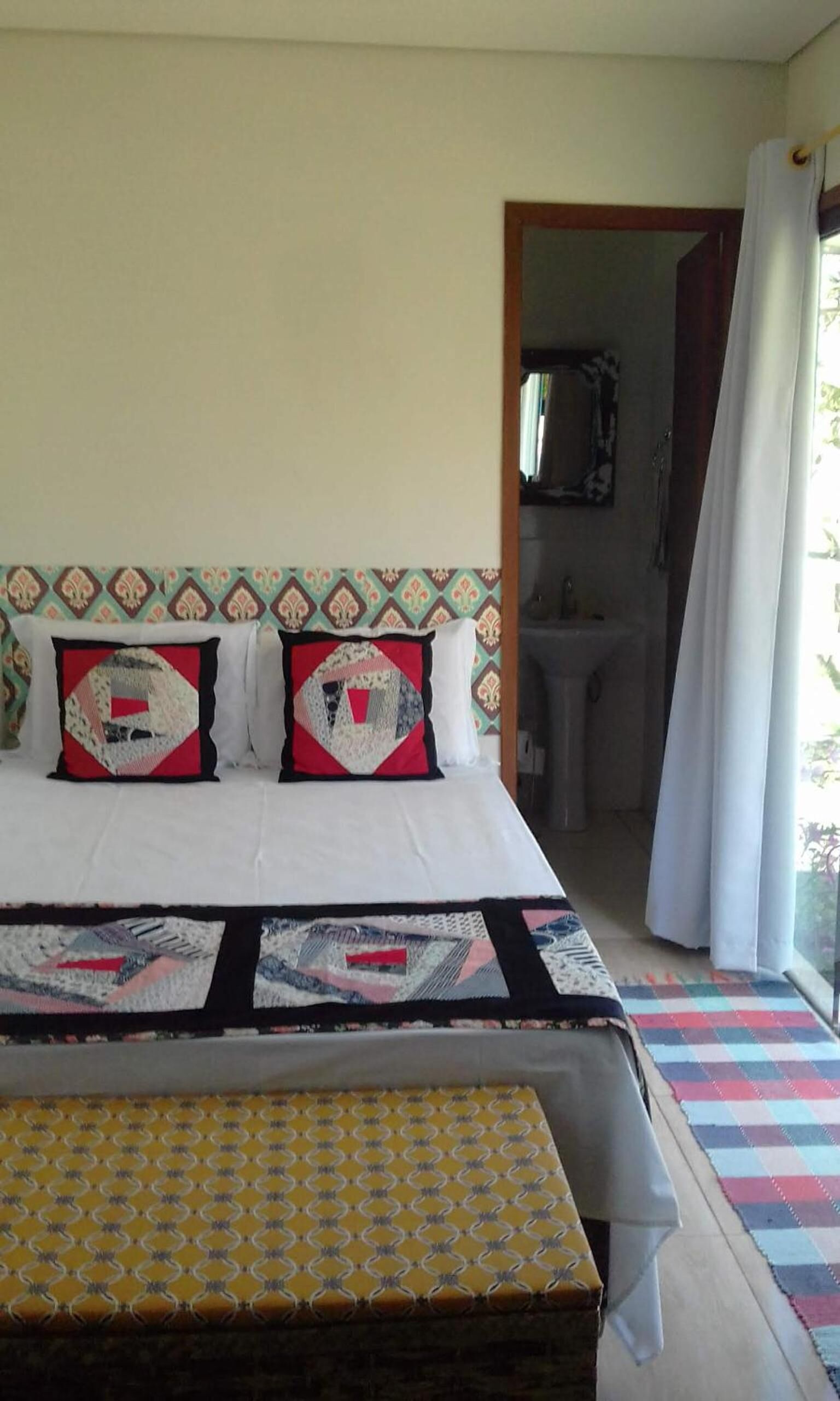 Una stanza con un letto, una panca, e un bagno parzialmente visibile attraverso una porta aperta, con un pavimento decorato.