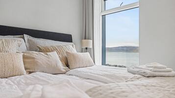 Una cama bien tendida con cabecera, almohadas y una lámpara al lado de una ventana con vistas.