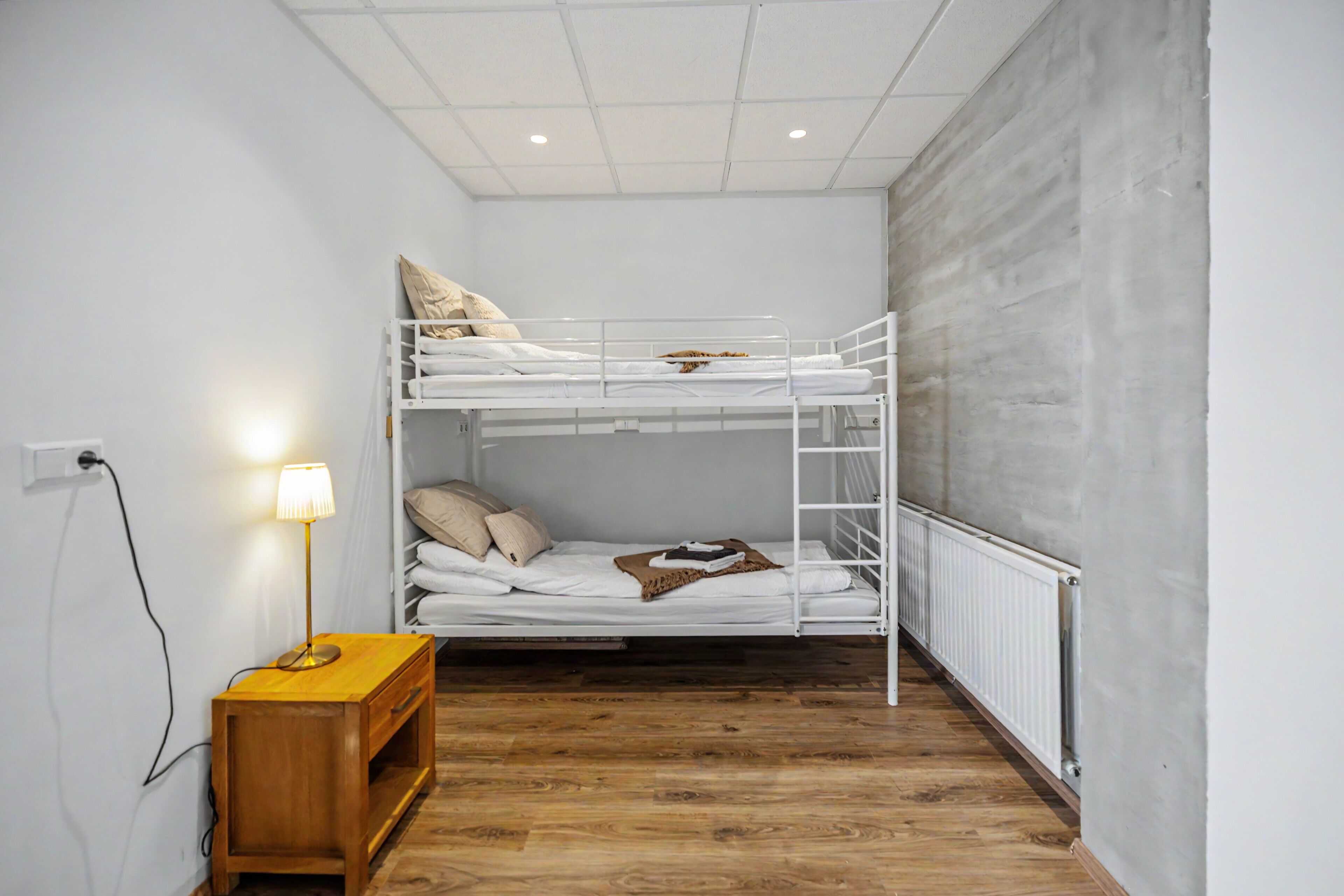 A bunk bed room with a wooden nightstand, a lamp, and a radiator.