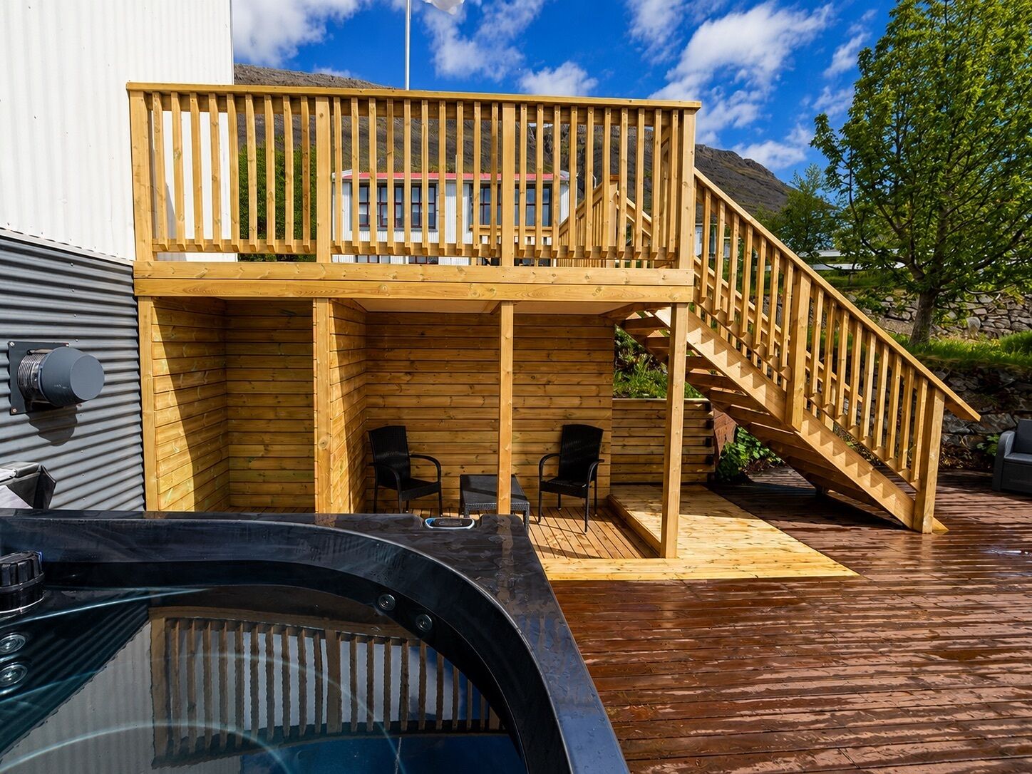 A two-story wooden deck with a hot tub, outdoor seating, and a staircase.