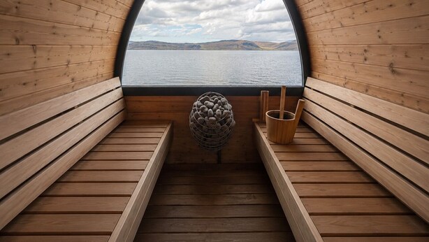 A sauna with wooden benches, a stone sculpture, and a view of a lake and mountains. - Hotel West (Vesturbyggð)