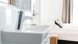 A modern bathroom with a white sink, chrome faucet, and a glass soap dispenser. - Hotel West (Vesturbyggð)