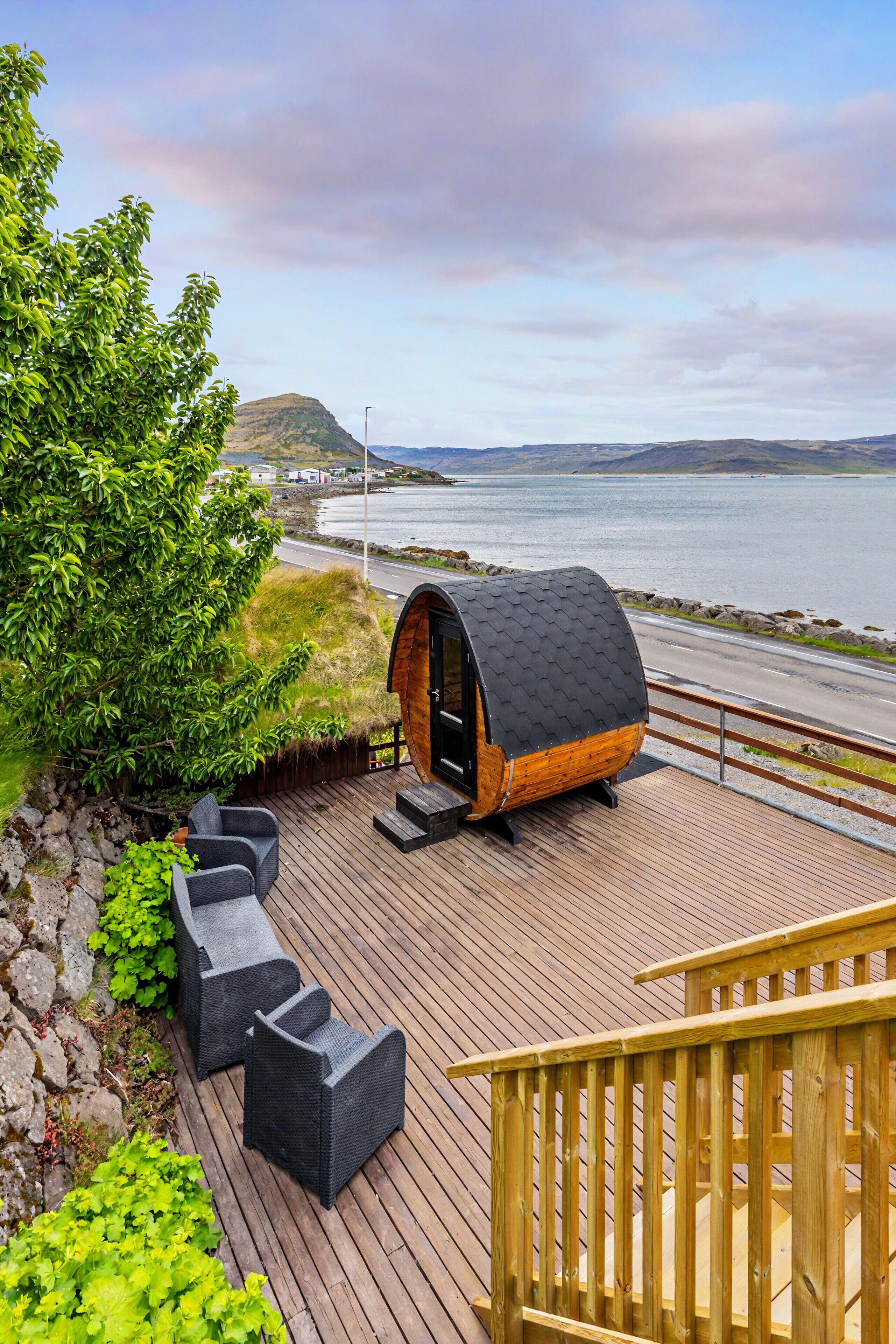 Une terrasse avec des sièges extérieurs et une structure en bois, offrant une vue sur un plan d’eau et des collines lointaines.