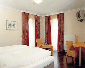 A hotel room with a bed, a small table with a chair, a television, and curtains.
