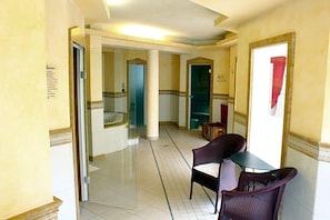 A hotel lobby with a tiled floor, a reception desk, and a seating area with chairs.