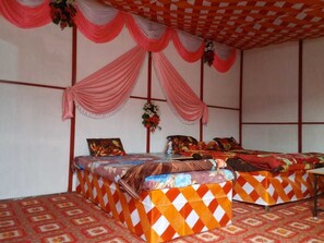 A room with two beds, each with patterned bedding and a table between them. - Krishna Kumbh Cottage (Prayagraj)