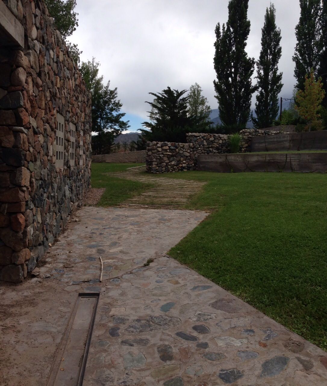A stone pathway leading to a grassy area with a stone wall and trees.