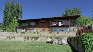 A modern two-story house with a stone retaining wall, large windows, and a well-maintained lawn.