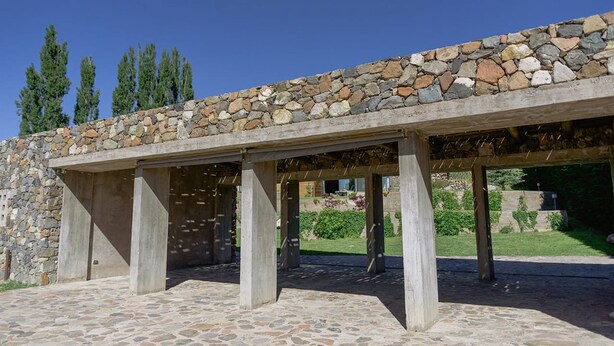 A stone-covered pergola structure with a stone wall and a tiled floor.