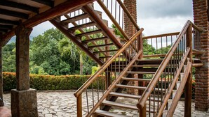 A wooden staircase with a metal railing, leading to a covered area with stone flooring and a view of lush greenery. - Hotel Beyonda (Santa Marta)