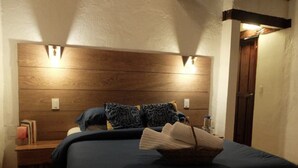 A bedroom with a wooden headboard, two bedside lamps, a bedside table with books, and a basket of folded towels. - Hotel Beyonda (Santa Marta)
