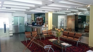 A hotel lobby with a reception desk, seating area, and a large mirror reflecting the space.
