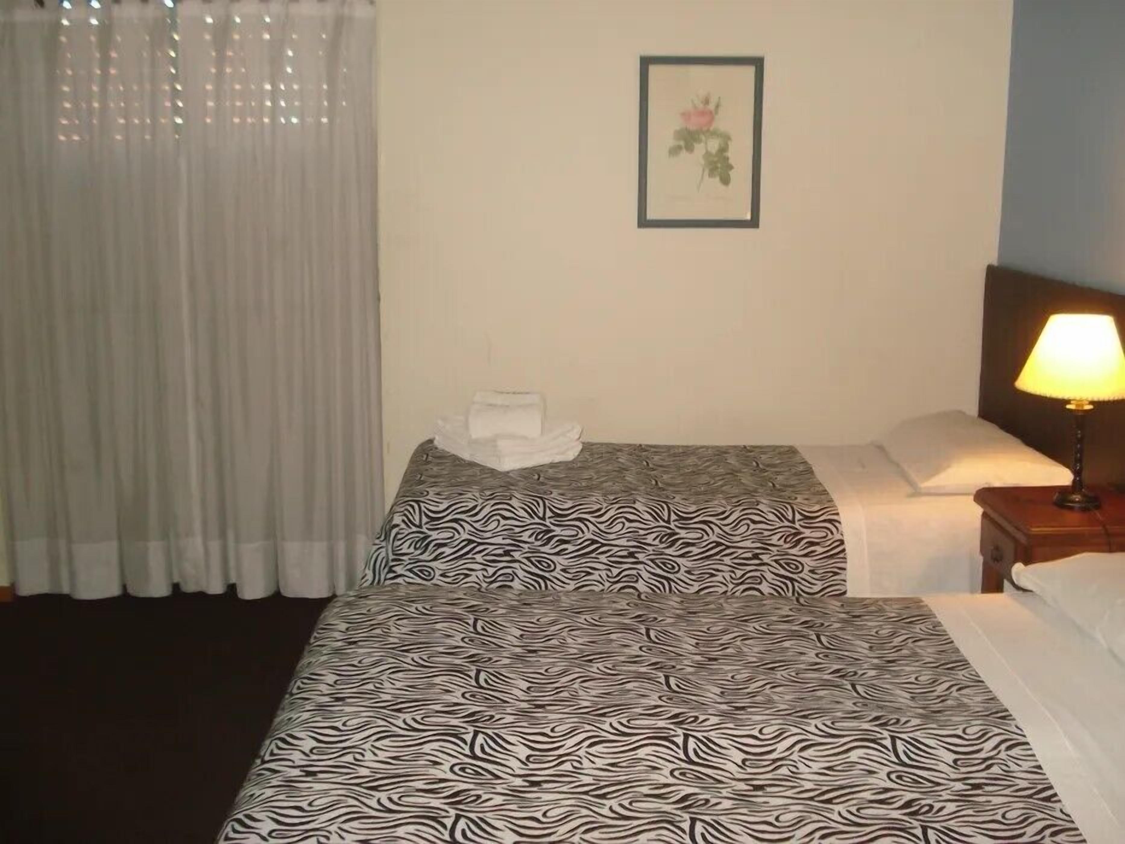 A hotel room with two beds, a nightstand with a lamp, a framed picture on the wall, and a window with curtains.